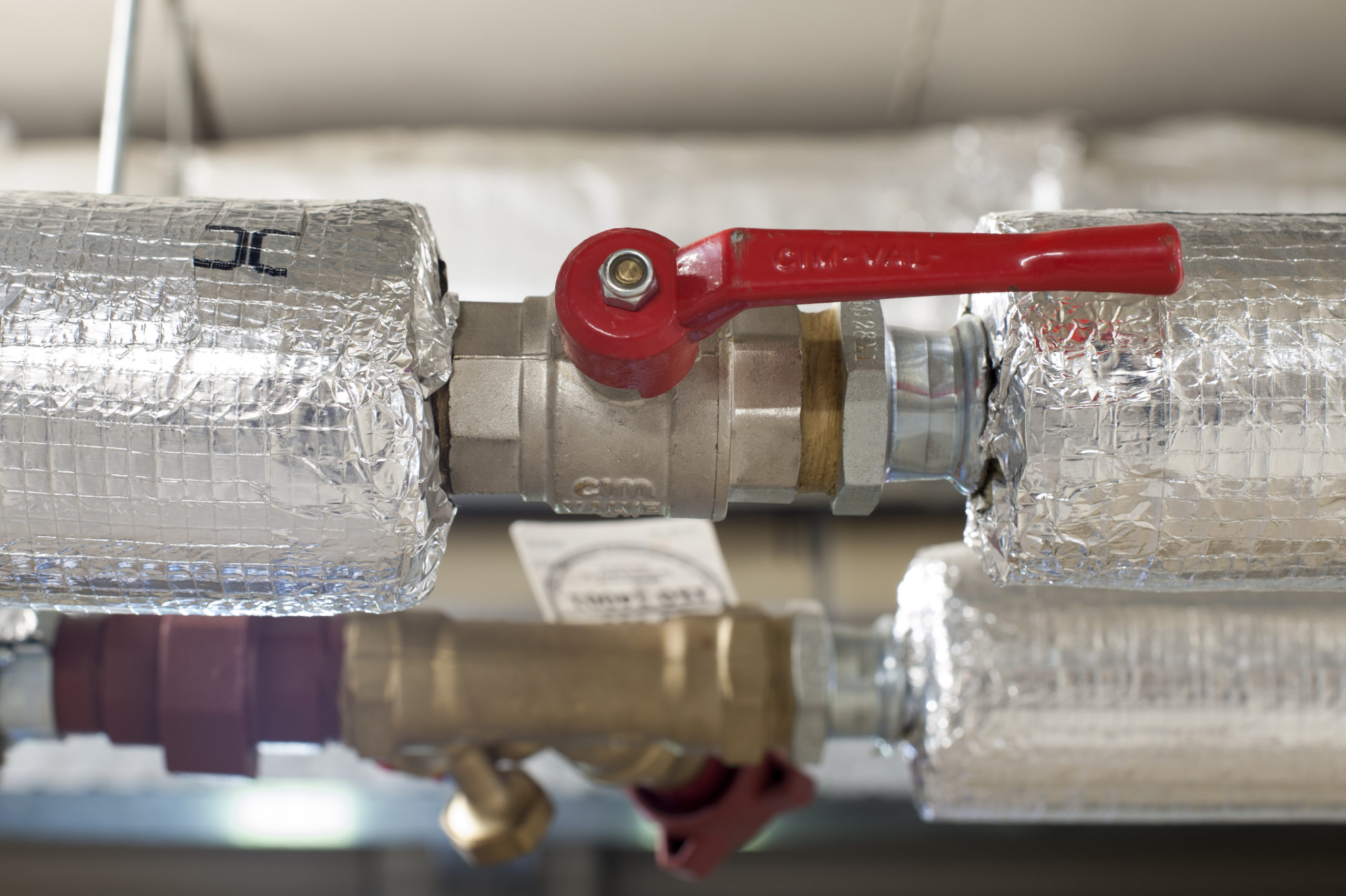Ball valve in an pipe of a central heating system Utrecht, The Netherlands - November 18, 2015: A red ball valve is located in a metal pipe covered with insulation material. The valve is used to control the flow of water and the pressure in a central heating systeem.